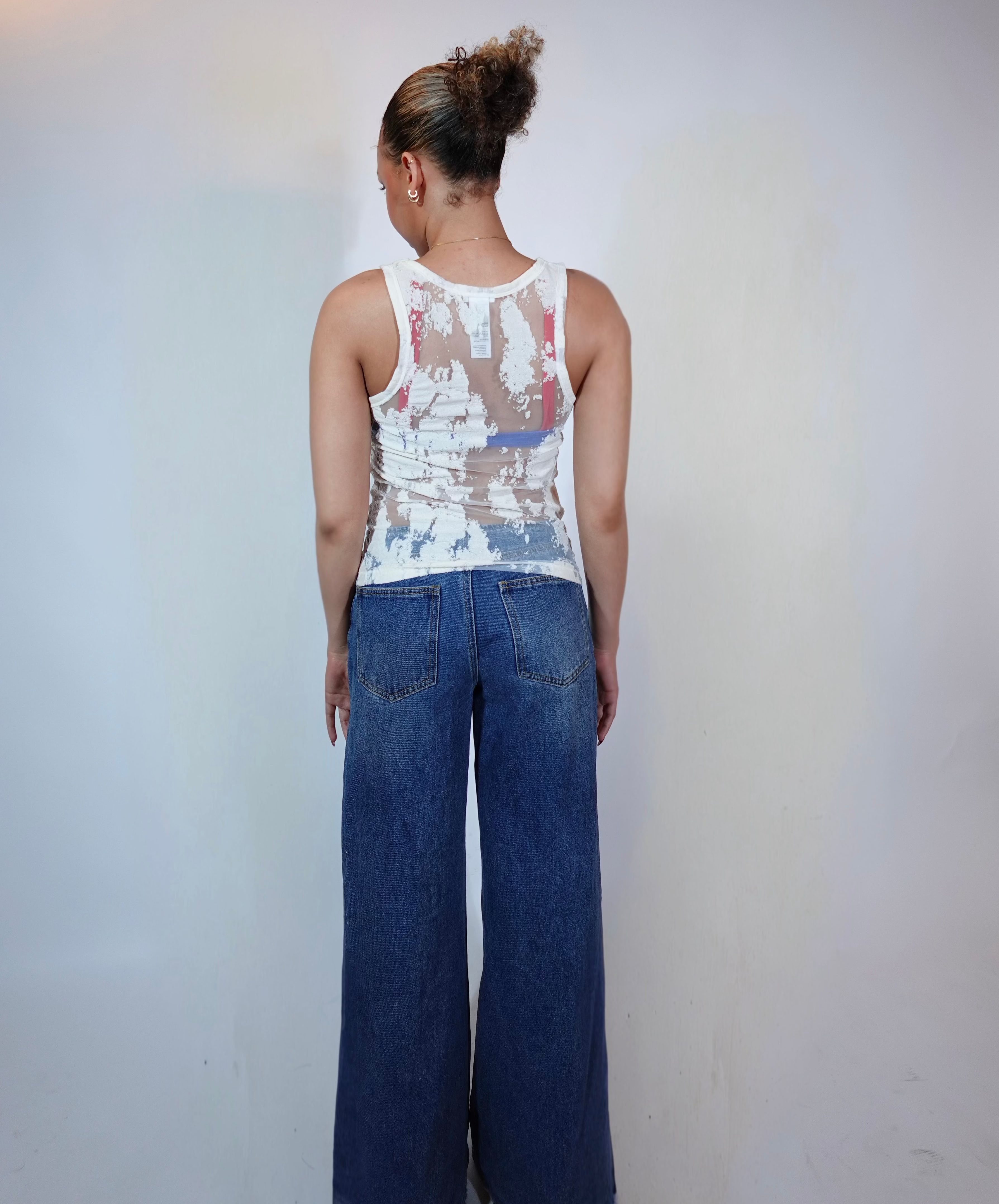 Person wearing a sleeveless top with abstract design and blue jeans against a plain background